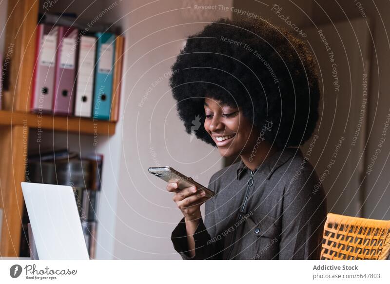 Fröhliche schwarze Frau beim Surfen auf dem Smartphone Browsen online Internet modern soziale Netzwerke Talkrunde Anschluss Laptop heimwärts Afroamerikaner