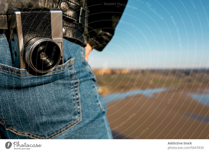 Detailansicht einer alten Kamera, die an der Jeans eines Reisenden befestigt ist Fotokamera altehrwürdig Fotografie reisen Abenteuer Fluss Landschaft Jeanshose