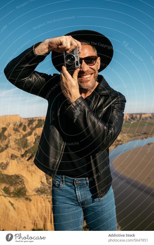 Stilvoller, fröhlicher Fotograf, der mit einer analogen Kamera Fotos im Freien macht Mann Glück Fotokamera altehrwürdig stylisch Hut Leder Jacke Hobby Freizeit