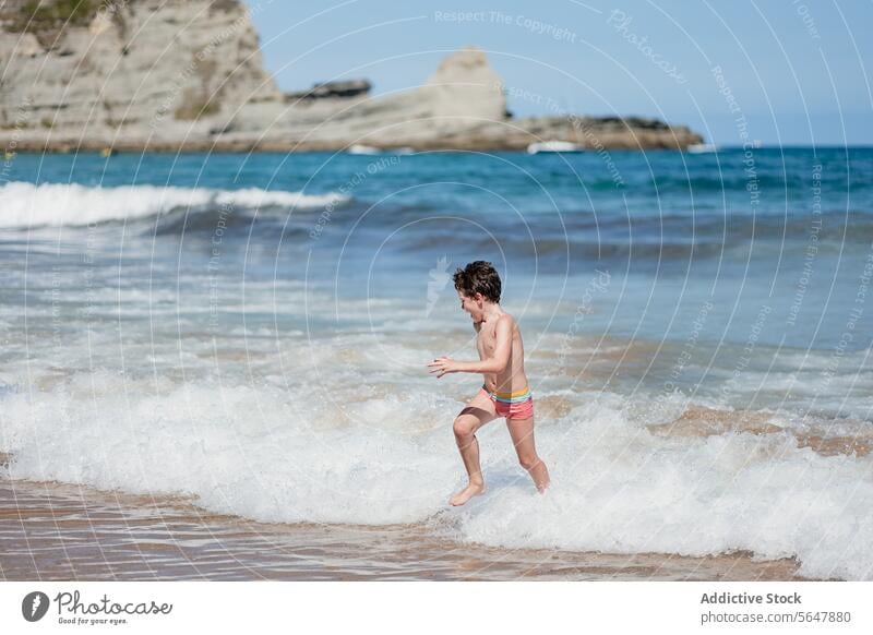 Kleiner Junge genießt spielerischen Lauf am sonnigen Strand laufen spielen winken Ufer Sand MEER Meer Sommer Spaß Kind im Freien Küste malerisch Natur Urlaub