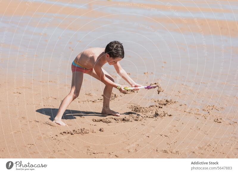 Kleiner Junge spielt mit einer Spielzeugschaufel am Sandstrand Strand spielen Meer Kind sandig Schürfen Seeküste Küste Sommer im Freien Aktivität sonnig
