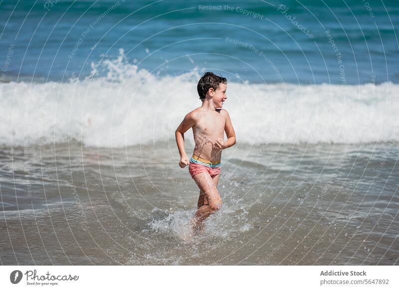 Junge spielt fröhlich in den Wellen des Meeres Kind Strand MEER winken platschen laufen Freude spielen Sommer sonnig Küste Glück Badebekleidung Urlaub Freizeit