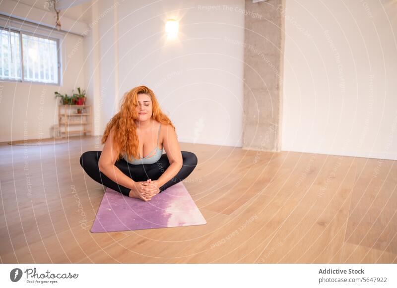 Konzentrierte junge plus size Frau übt Yoga-Asana auf der Matte im Yoga-Studio Konzentration üben Sportbekleidung Dame Übergröße Unterlage Training sitzen