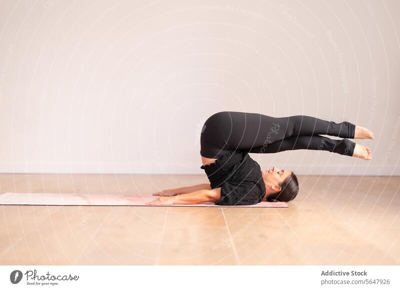 Flexible Frau übt Yoga-Pose in einem geräumigen Zimmer Dame üben Sportkleidung Wegbiegung Dehnung Training beweglich passen Unterlage Übung Atelier Gesundheit