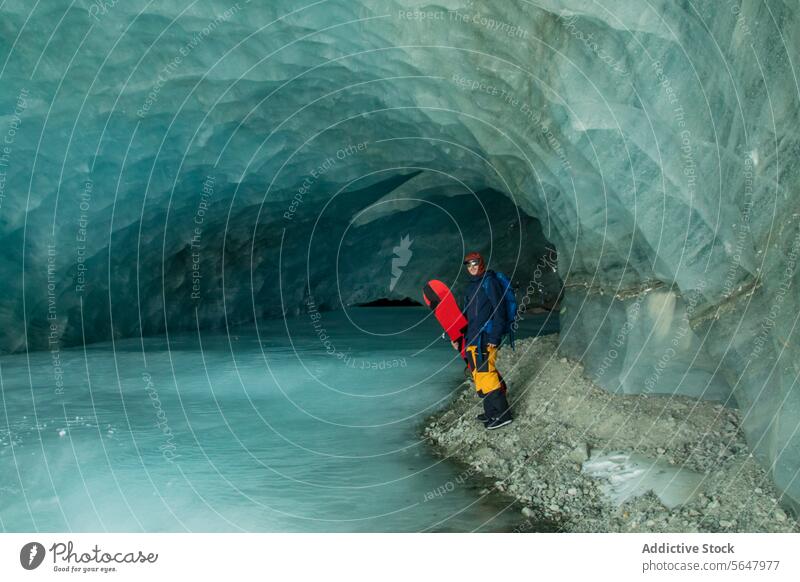 Aktive Person erkundet Eishöhle im Winter Tourist Höhle Abenteuer Urlaub erkunden Seitenansicht unkenntlich aktiv Rucksack Snowboard Spaziergang gefroren Fluss