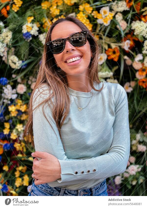 Frau lächelnd gegen eine bunte Blume Hintergrund Sonnenbrille Lächeln Blumen Halskette heiter pulsierend farbenfroh geblümt Schönheit Großstadt Straße Freude