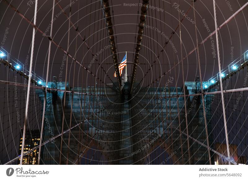 Beleuchtete Brooklyn Bridge mit amerikanischer Flagge bei Nacht, Manhattan Brücke beleuchtet Fahne Amerikaner Wahrzeichen Architektur Struktur Großstadt urban
