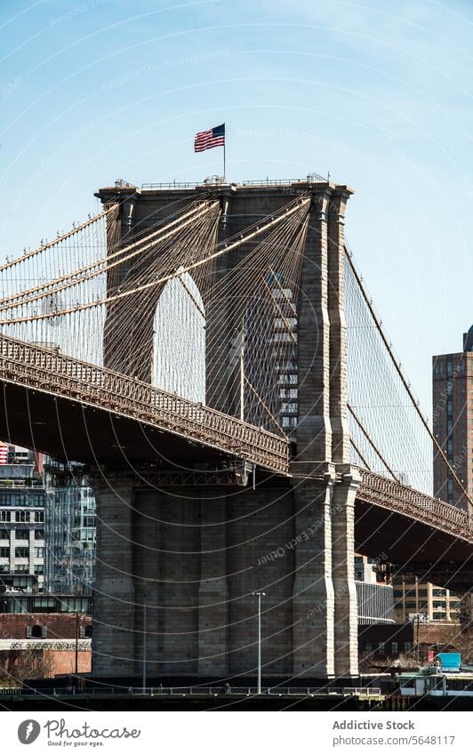 Turm der Brooklyn Bridge mit wehender amerikanischer Flagge vor blauem Himmel. Brücke Amerikaner Fahne Architektur kultig Wahrzeichen New York State Kabel Stein