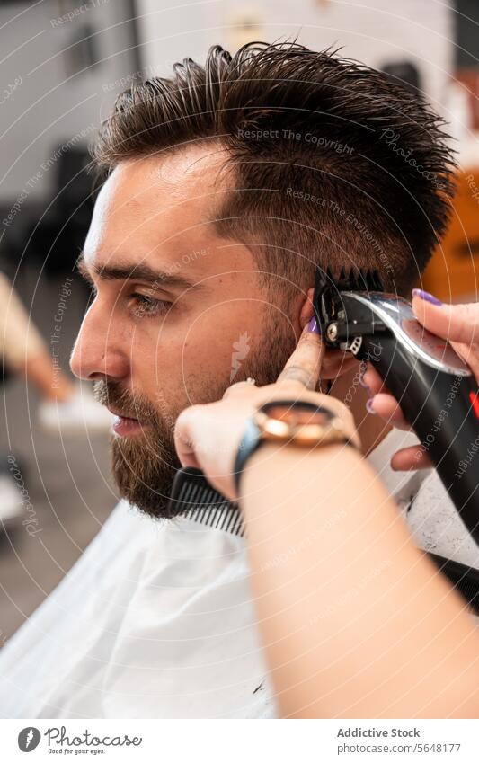 Abgeschnittene, nicht erkennbare Friseurin bei der Verwendung eines elektrischen Trimmers an den Haaren eines männlichen Kunden im Salon Mann Behaarung Pflege