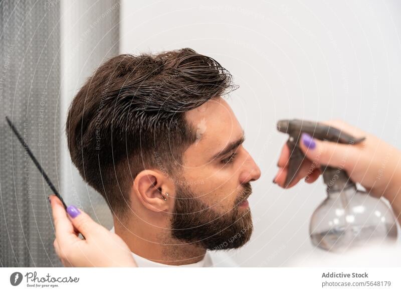 Abgeschnittene Hände einer nicht erkennbaren Friseurin, die Wasser auf das Haar eines männlichen Kunden im Salon sprüht Spray Mann Behaarung Pflege nass Dienst