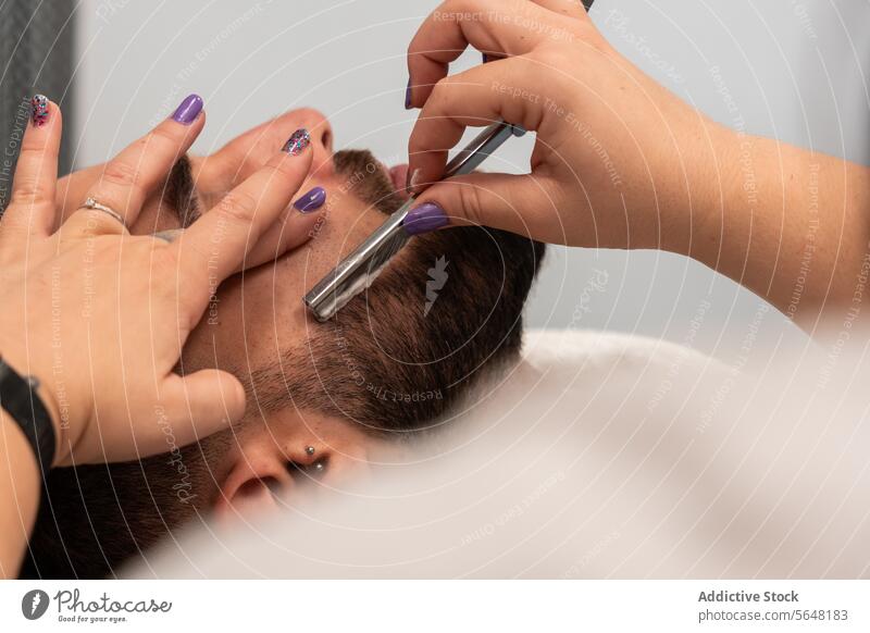 Unkenntlich gemachte Hände einer Friseurin, die den Bart eines männlichen Kunden mit einem Rasiermesser rasiert, in einem Salon Rasieren Gerades Rasiermesser