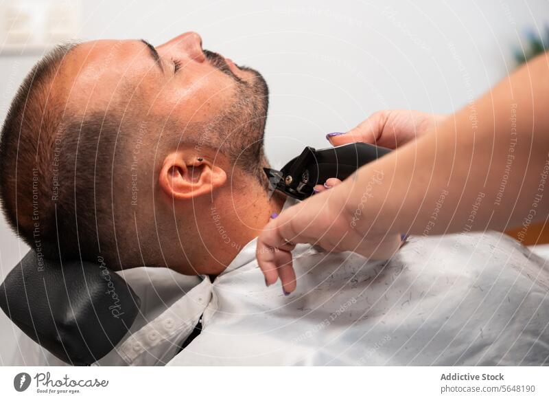 Seitenansicht einer abgeschnittenen, nicht erkennbaren Friseurin, die den Bart eines männlichen Kunden mit einem Trimmer rasiert Rasieren Vollbart Mann Salon