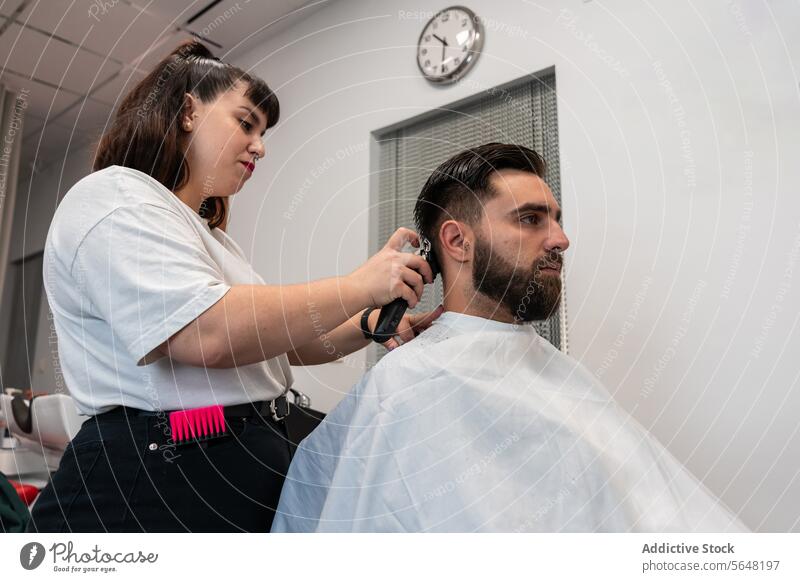 Seitenansicht einer Friseurin bei der Anwendung eines elektrischen Trimmers an den Haaren eines männlichen Kunden im Salon Mann Behaarung Pflege Dienst Hand