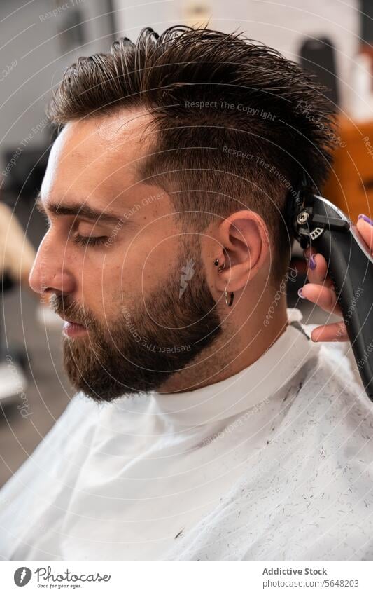 Abgeschnittene, nicht erkennbare Friseurin bei der Verwendung eines elektrischen Trimmers an den Haaren eines männlichen Kunden im Salon Mann Behaarung Pflege