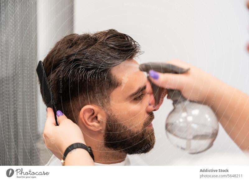 Abgeschnittene Hände einer nicht erkennbaren Friseurin, die Wasser auf das Haar eines männlichen Kunden im Salon sprüht Spray Mann Behaarung Pflege nass Dienst