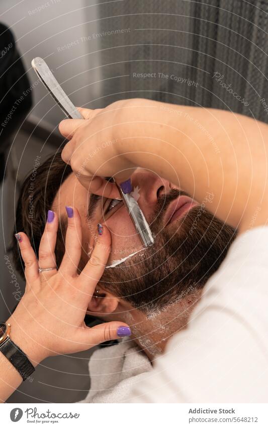 Von oben Ernte unerkennbar Hände der weiblichen Friseur rasieren männlichen Kunden den Bart mit Rasiermesser im Salon Rasieren Gerades Rasiermesser Vollbart