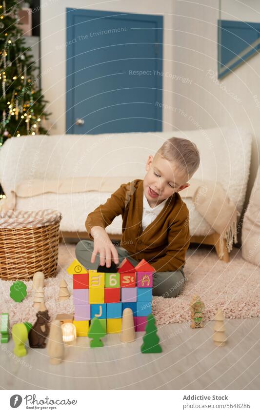 Kleiner Junge spielt mit Blöcken im Wohnzimmer vor dem Weihnachtsbaum Weihnachten Kind Spielzeit farbenfroh Teppich glühen Baum Feiertag Saison Unschuld Spaß