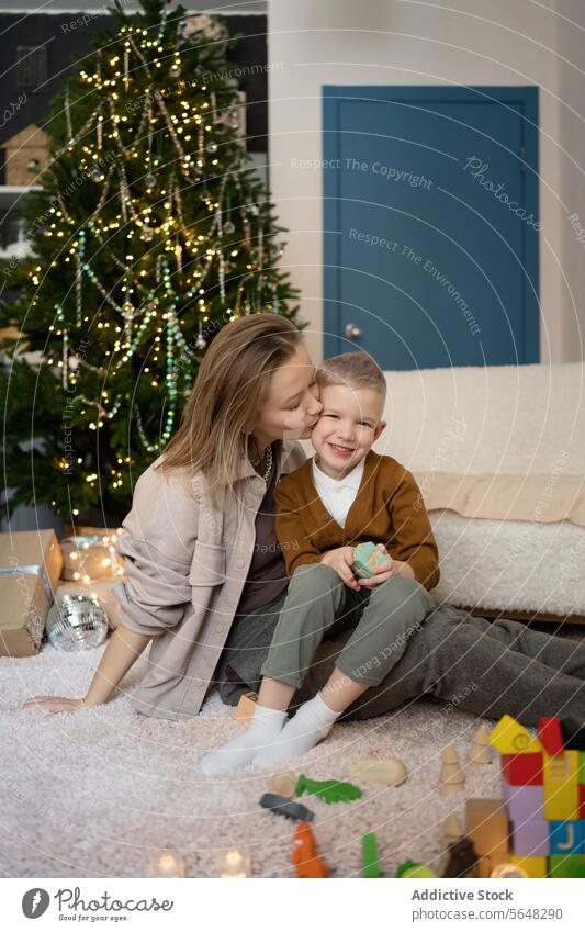 Mutter küsst ihren Sohn und spielt zusammen mit Holzspielzeug im Wohnzimmer vor dem Weihnachtsbaum Kind Weihnachten Freude lachen festlich Saison Baum Spielen