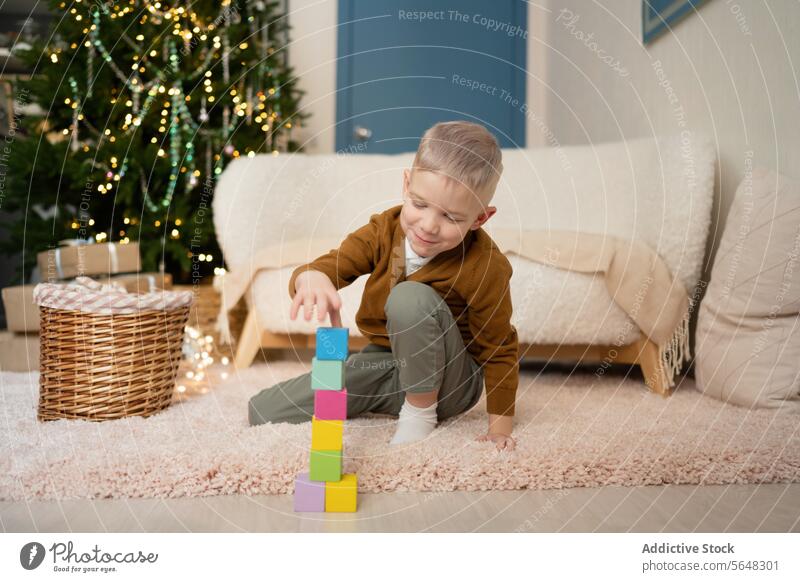 Kleiner Junge spielt mit Blöcken im Wohnzimmer vor dem Weihnachtsbaum Weihnachten Kind Spielzeit farbenfroh Teppich glühen Baum Feiertag Saison Unschuld Spaß