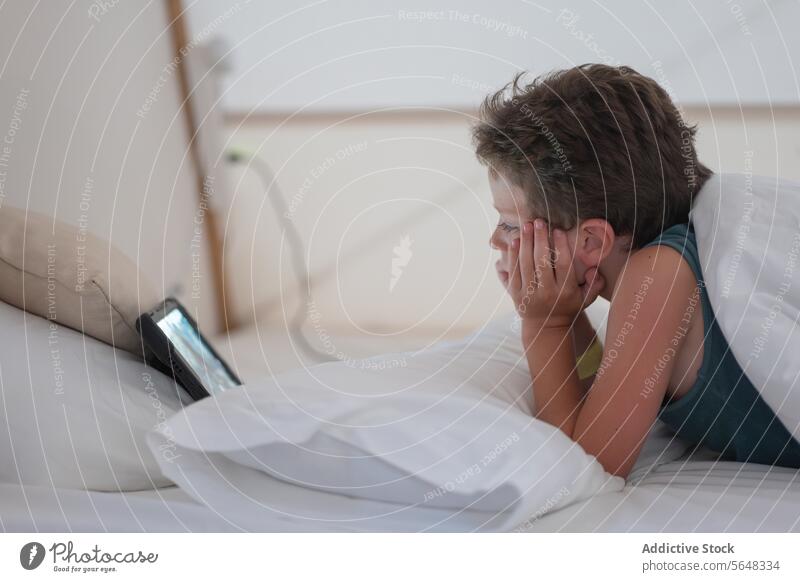 Kleiner Junge sieht sich ein Video auf einem Tablet an, während er im Schlafzimmer liegt Tablette zuschauen ruhen Kind Internet Decke sich[Akk] entspannen