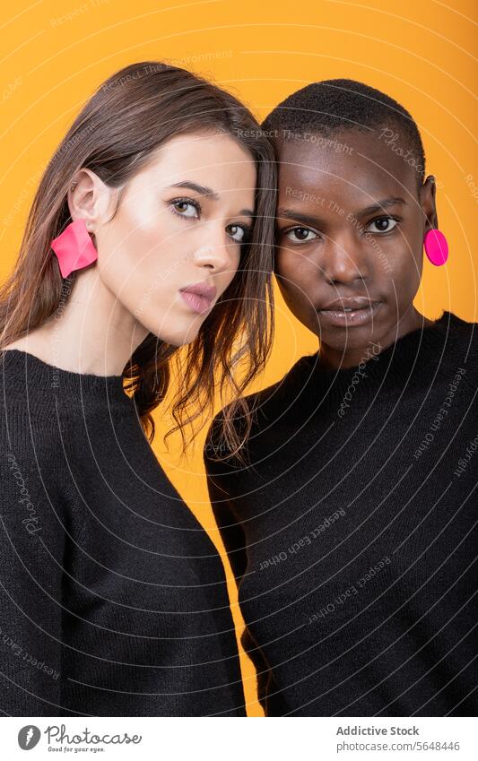 Diverse junge Freundinnen tragen rosa Ohrringe Frauen vielfältig selbstbewusst Porträt trendy T-Shirt Zusammensein rassenübergreifend Freizeitkleidung posierend