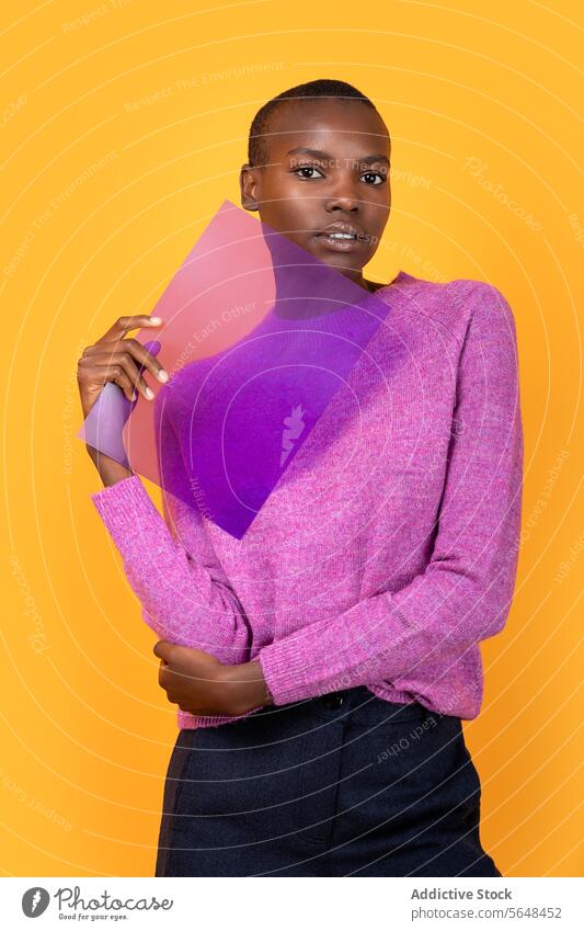 Schwarze Frau in warmer Kleidung hält transparenten Kunststoff auf gelbem Hintergrund Beteiligung purpur Pullover vereinzelt Afroamerikaner Textfreiraum Porträt