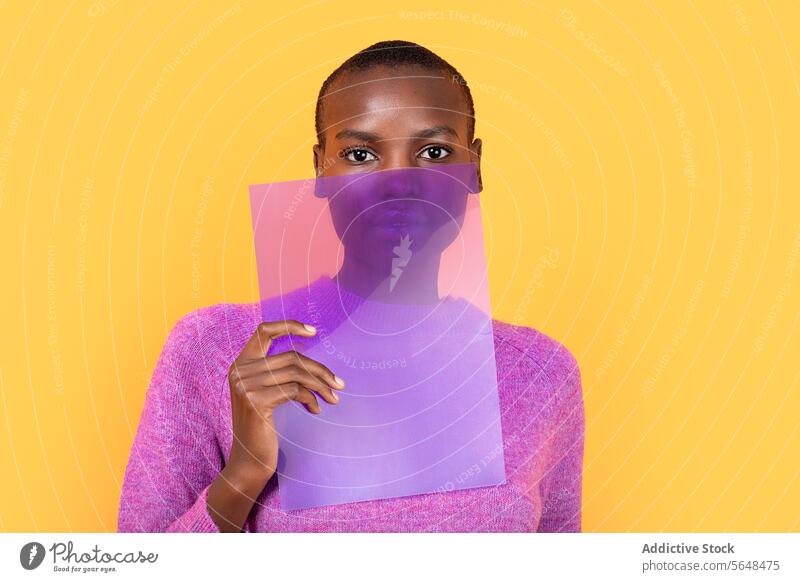 Schwarze Frau in warmer Kleidung hält transparenten Kunststoff auf gelbem Hintergrund Beteiligung purpur Pullover vereinzelt Afroamerikaner Textfreiraum Porträt