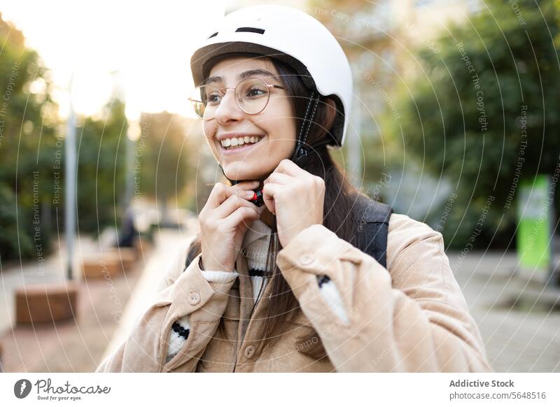 Lächelnde Frau, die den Helmgurt im Freien befestigt Schutzhelm Sicherheit Befestigung Mitfahrgelegenheit Gurt heiter jung Erwachsener Vorbereitung sicheres