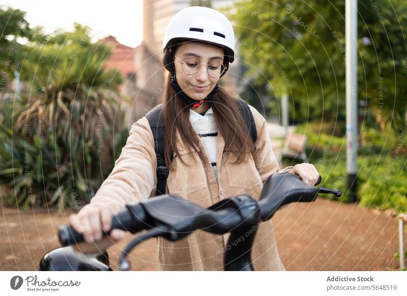Junge Frau bereitet sich auf das Fahren eines Elektrorollers vor Schutzhelm Freizeitkleidung Transport umweltfreundlich sonniger Tag Mitfahrgelegenheit