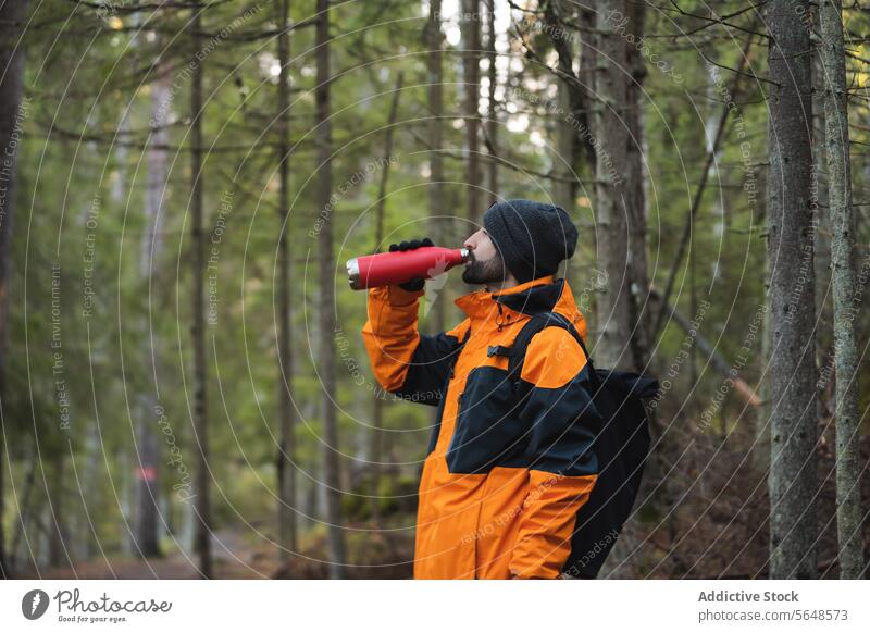 Männlicher Forscher im Regenmantel, der im Wald Wasser aus einer Flasche trinkt Mann Wanderer Trekking Wanderung trinken Park Entdecker Wälder Natur Tourismus