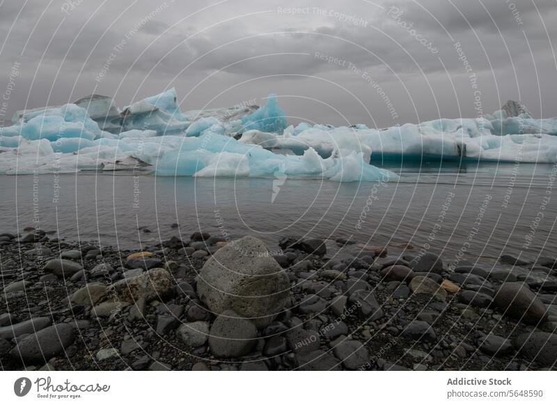 Eisberge schwimmen in einer Gletscherlagune unter einem bewölkten Himmel mit glatten Kieselsteinen im Vordergrund an der Küste in Island Lagune glazial wolkig