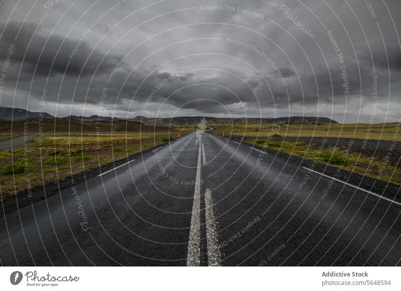Eine offene Straße erstreckt sich bis zum Horizont unter einem düsteren Himmel in einer trostlosen isländischen Landschaft Island stürmisch desolat reisen