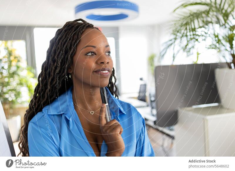 Nachdenkliche junge afroamerikanische Geschäftsfrau, die einen Marker hält, während sie im Büro steht Markierung nachdenklich Präsentation Brainstorming Lächeln