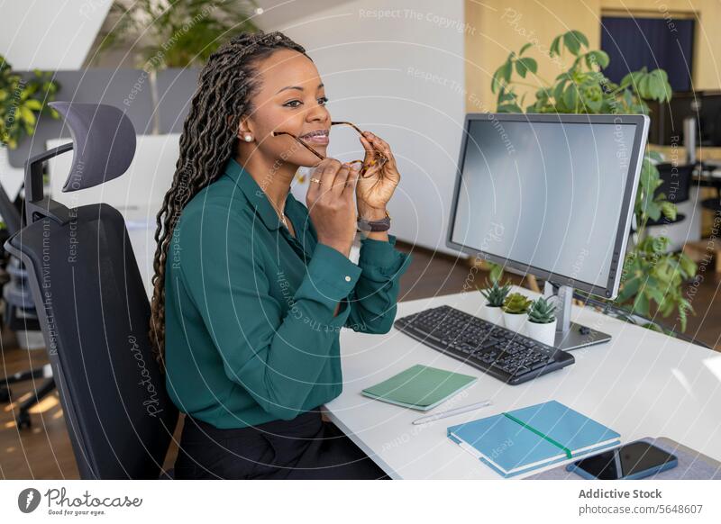 Geschäftsfrau beim Aufsetzen der Brille am Computer im Büro angezogen Schreibtisch Arbeitsplatz Afro-Look Monitor Textfreiraum Unternehmer Business Beruf