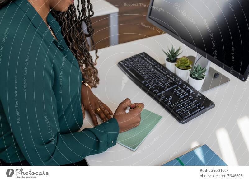 Von oben junge afroamerikanische Geschäftsfrau beim Schreiben auf einem Notizblock am Computer im Büro schreiben Schreibtisch Keyboard von oben Schreibstift
