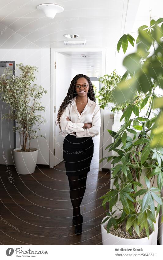 Porträt einer glücklichen schwarzen Geschäftsfrau mit verschränkten Armen im Büro Glück selbstbewusst Erfolg formal die Arme verschränkt Lächeln Ganzkörper Frau