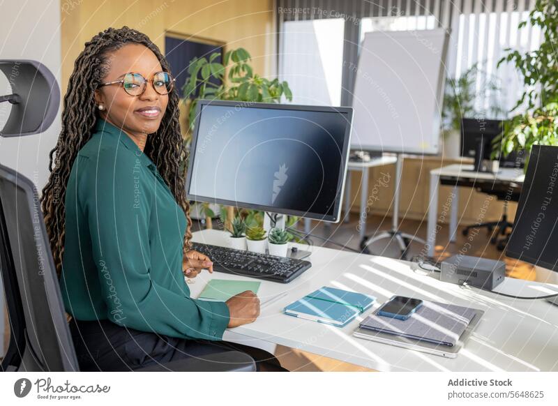 Glückliche Geschäftsfrau sitzt am Computer im Büro Porträt Schreibtisch selbstbewusst Lächeln Monitor Brille Arbeitsplatz Afro-Look Textfreiraum Unternehmer