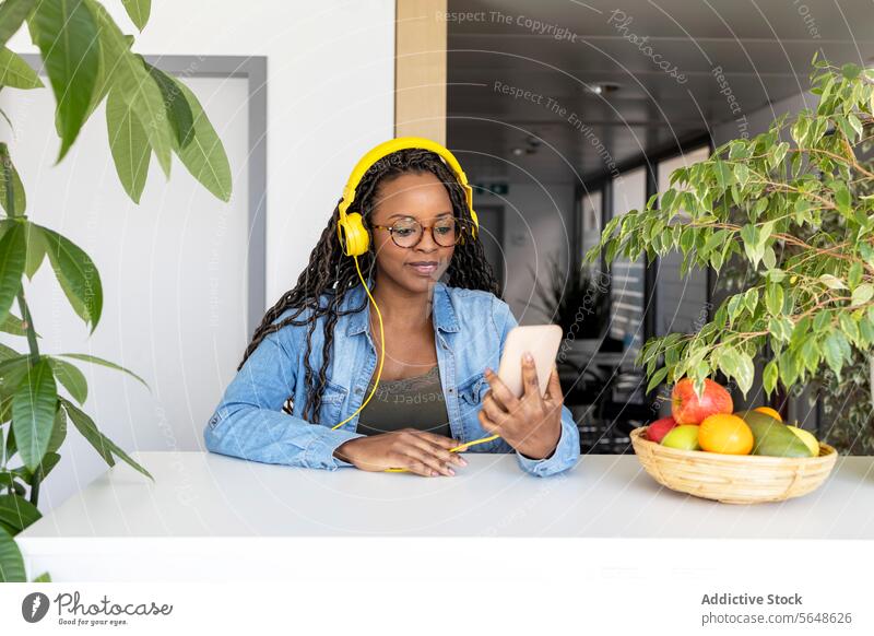 Geschäftsfrau mit Kopfhörern und Smartphone im Kreativbüro benutzend Büro Musik Lächeln gelb modern kreativ Frucht Schreibtisch Arbeit Business Beruf Gerät
