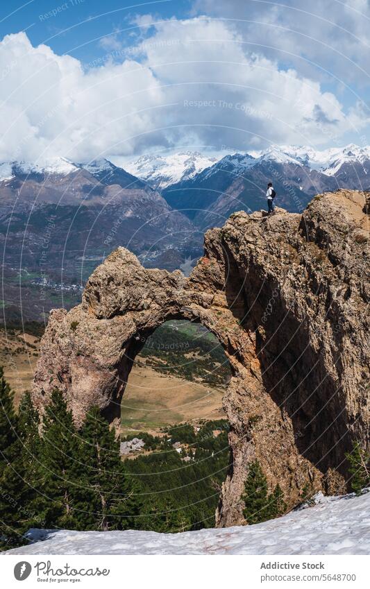 Wanderer blickt durch einen natürlichen Felsbogen auf schneebedeckte Gipfel natürlicher Bogen Gesteinsformationen Pyrenäen Berge u. Gebirge Schnee Natur