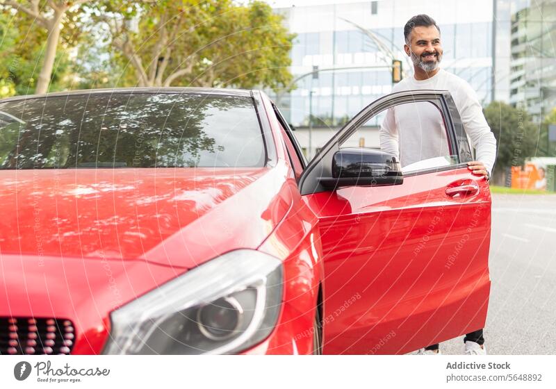 Erfreulicher ethnischer Fahrer, der auf der Straße in ein rotes Auto steigt Geschäftsmann Automobil Laufwerk PKW Autoreise Mitfahrgelegenheit Unternehmer