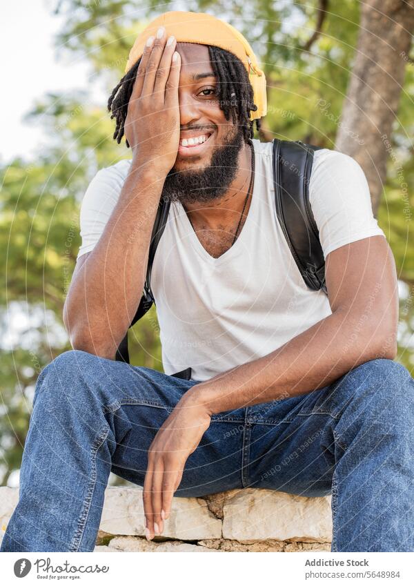 Fröhlicher schwarzer Mann bedeckt Auge im Park Hipster Auge abdecken Deckblatt Hälfte zuhören Musik Kopfhörer Sommer Lächeln Glück cool heiter männlich jung