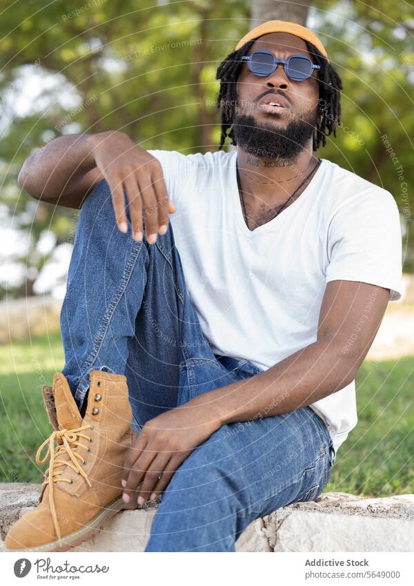 Selbstbewusster männlicher Hipster sitzt im Park Mann selbstbewusst cool informell Streetstyle Borte ruhen Sommer selbstsicher jung Afroamerikaner schwarz