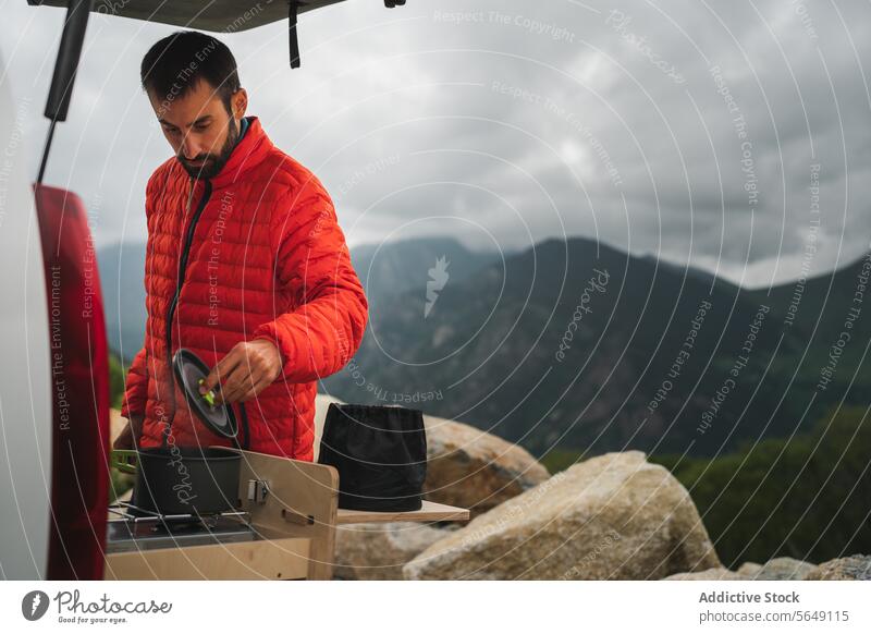 Mann in Winterjacke kocht Essen beim Wandern auf dem Lande Wanderer Koch Lebensmittel Herd Container Berge u. Gebirge Natur vorbereiten Abenteuer Nationalpark