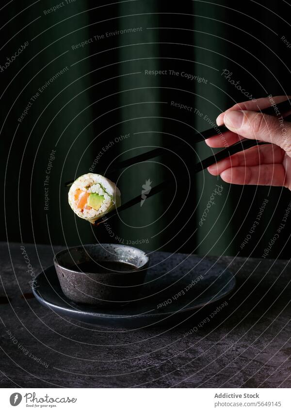 Sushi-Rolle in Stäbchen mit Sauce Tropf über Schüssel auf dem Tisch vor grünem Hintergrund rollen Nahaufnahme Essstäbchen Saucen Tröpfchen Textur kulinarisch