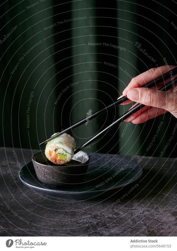 Sushi-Rolle mit Stäbchen gehalten über Sauce vor grünem Hintergrund rollen Essstäbchen Hand Saucen Soja Schalen & Schüsseln elegant dunkel frisch Zutaten
