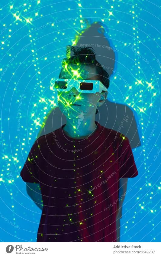 Niedliches Kind mit 3D-Brille im Neonstudio mit blauen und grünen Lichtern Junge 3d glühen neonfarbig unterhalten sorgenfrei futuristisch leuchten Kindheit