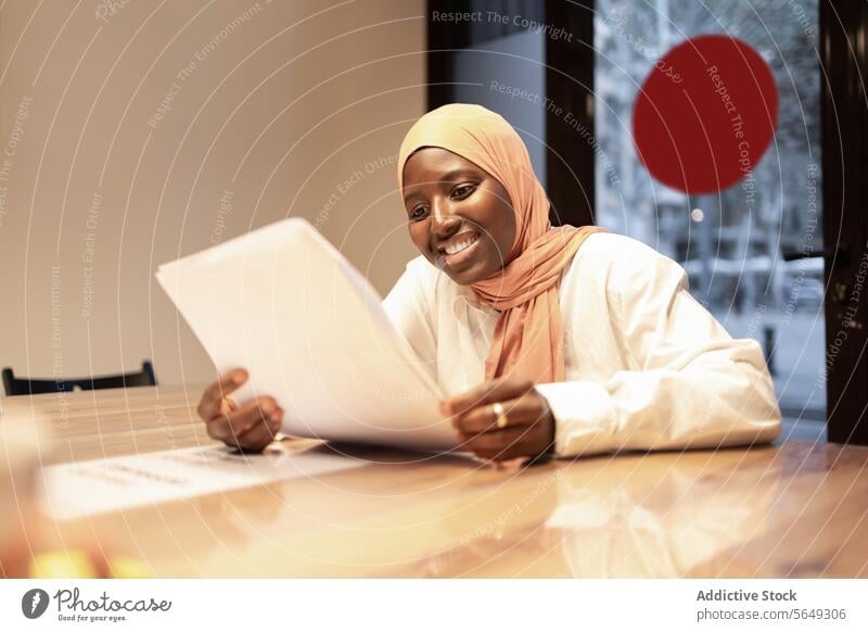 Glückliche islamische Frau beim Lesen von Papierdokumenten Papierkram Lächeln Schriftstück Hijab lesen Arbeit Kopftuch Projekt Büro Unternehmer Beruf Tisch