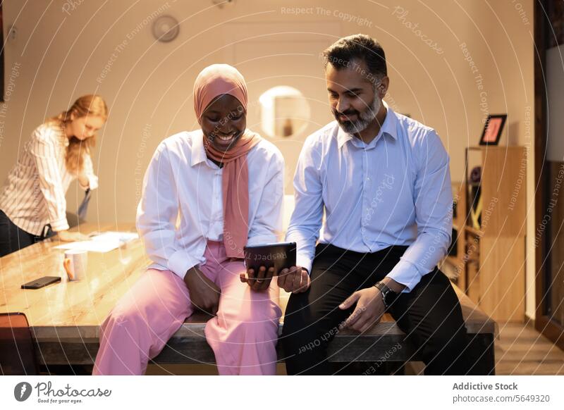 Lächelnde ethnische Kollegen, die in einem modernen Büro auf ein Tablet schauen Tablette Projekt Mitarbeiterin benutzend Browsen diskutieren Gerät Business