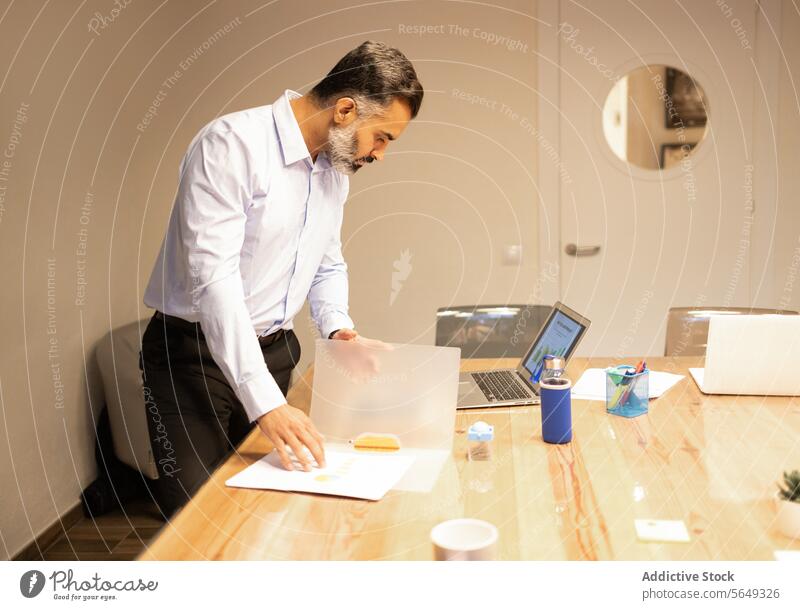 Konzentrierter Geschäftsmann, der Dokumente in der Nähe des Laptops am Tisch im Büro überprüft Mann professionell Papierkram Schriftstück Netbook Unternehmer