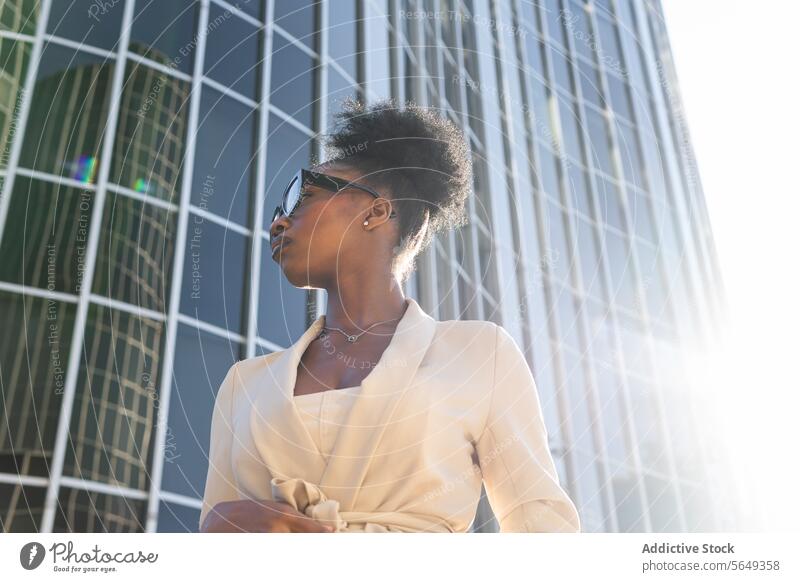 Niedriger Winkel der schwarzen modischen Unternehmer mit Brille Blick weg gegen Gebäude in der Stadt Manager stylisch niedriger Winkel Großstadt Sonnenlicht